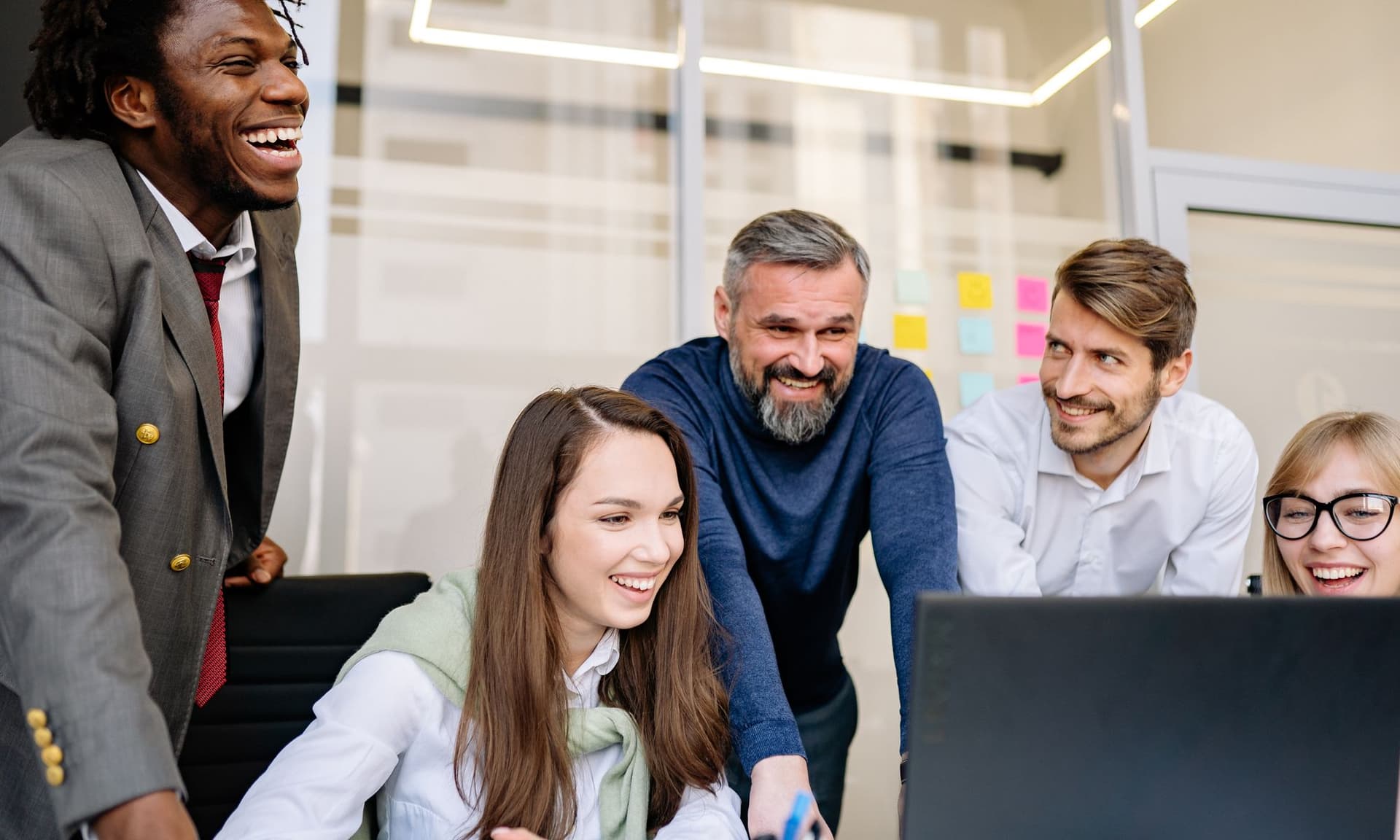 A diverse team laughing together around a laptop in a bright, modern office