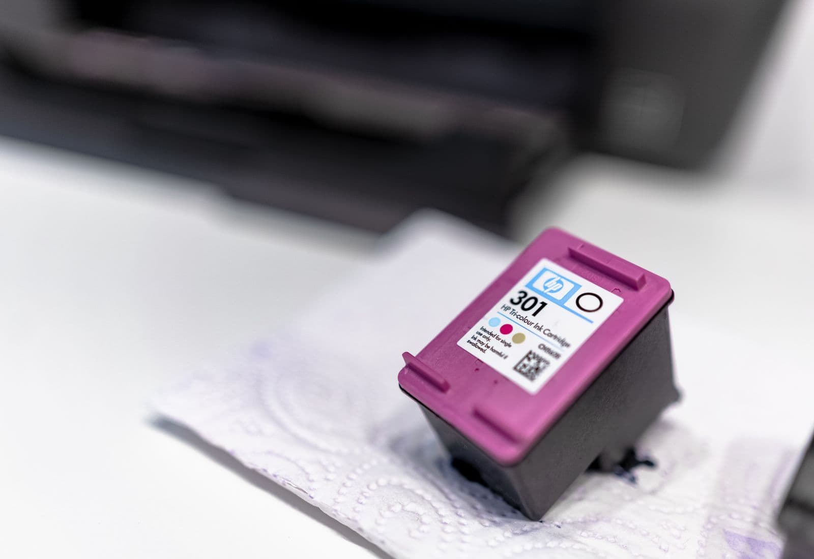 A colour ink cartridge on a desk beside an office printer